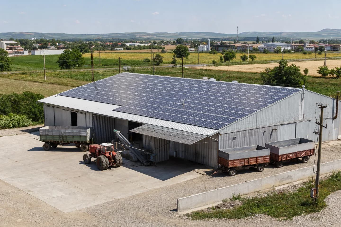 Hală agricolă din România cu panouri fotovoltaice, tractor și remorci pentru cereale